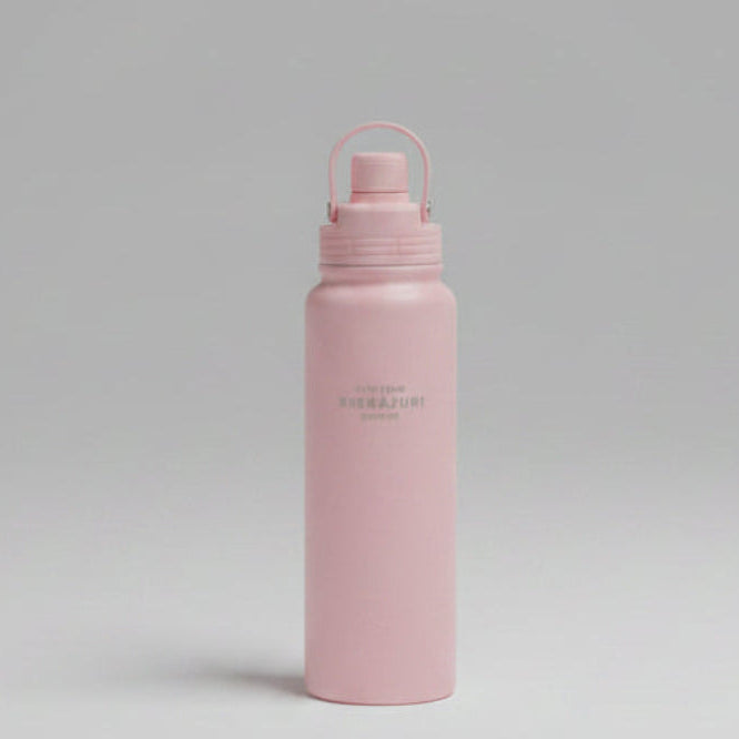 A matte pink water bottle with a matching pink lid and carrying loop, featuring the brand name 'NATURE SITAYURI' printed vertically in gold. The bottle is placed horizontally on a textured green artificial grass surface.